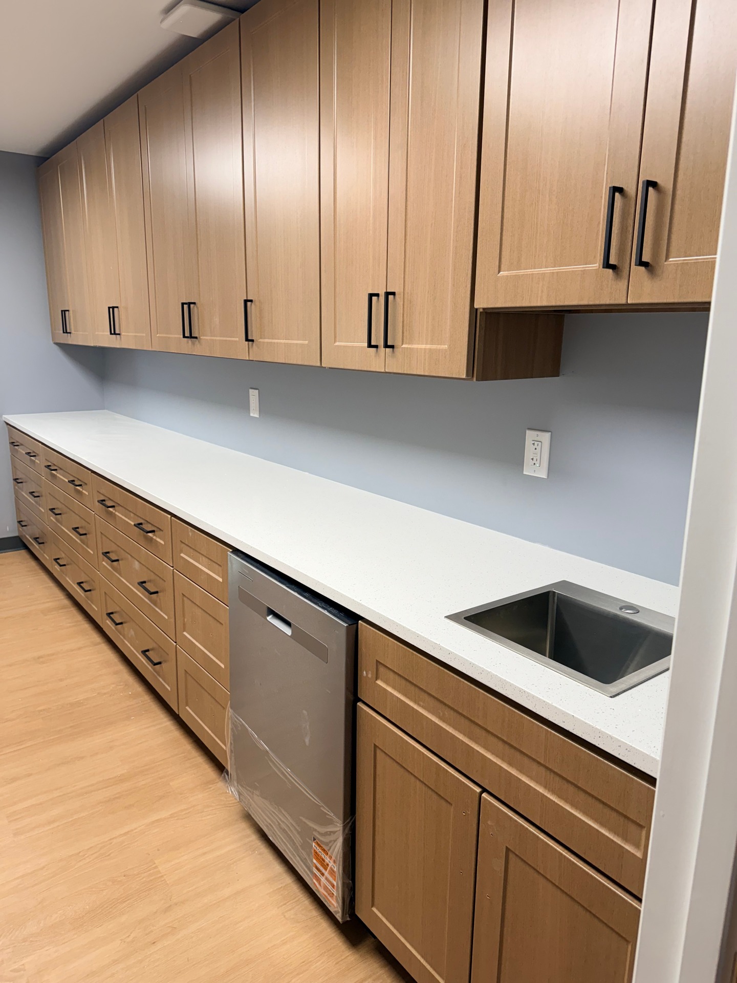 Wood cabinets and a white countertop with a stainless steel sink and dishwasher in a kitchen.