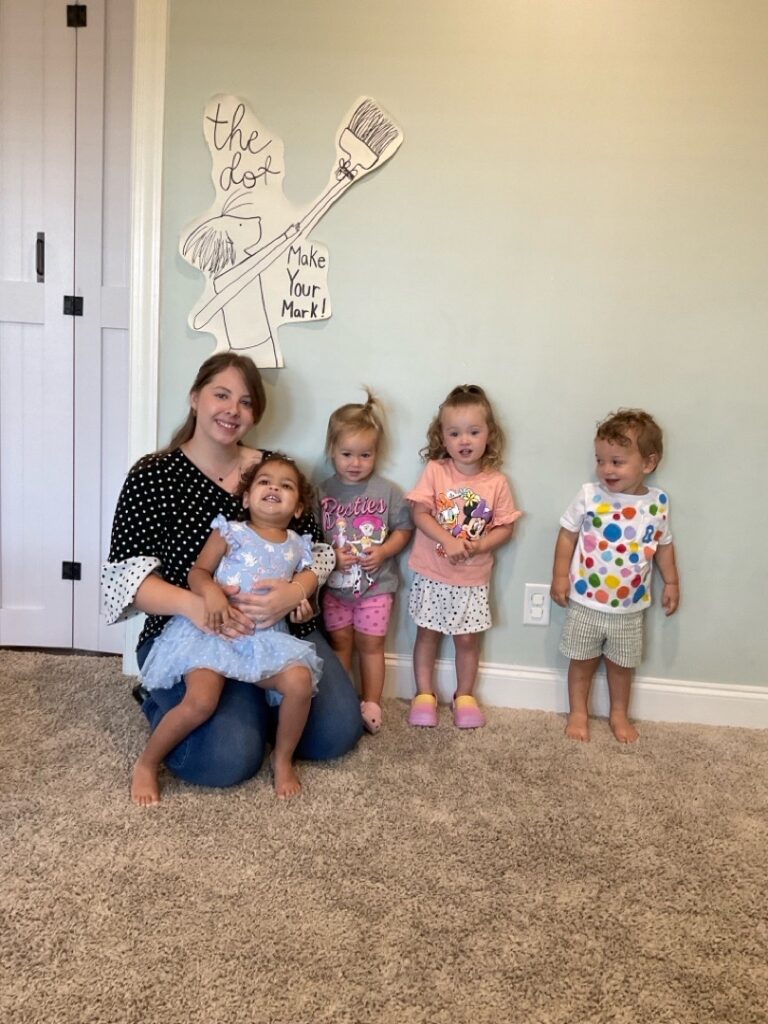 A Corky teacher sitting on the floor with a group of toddlers in their classroom