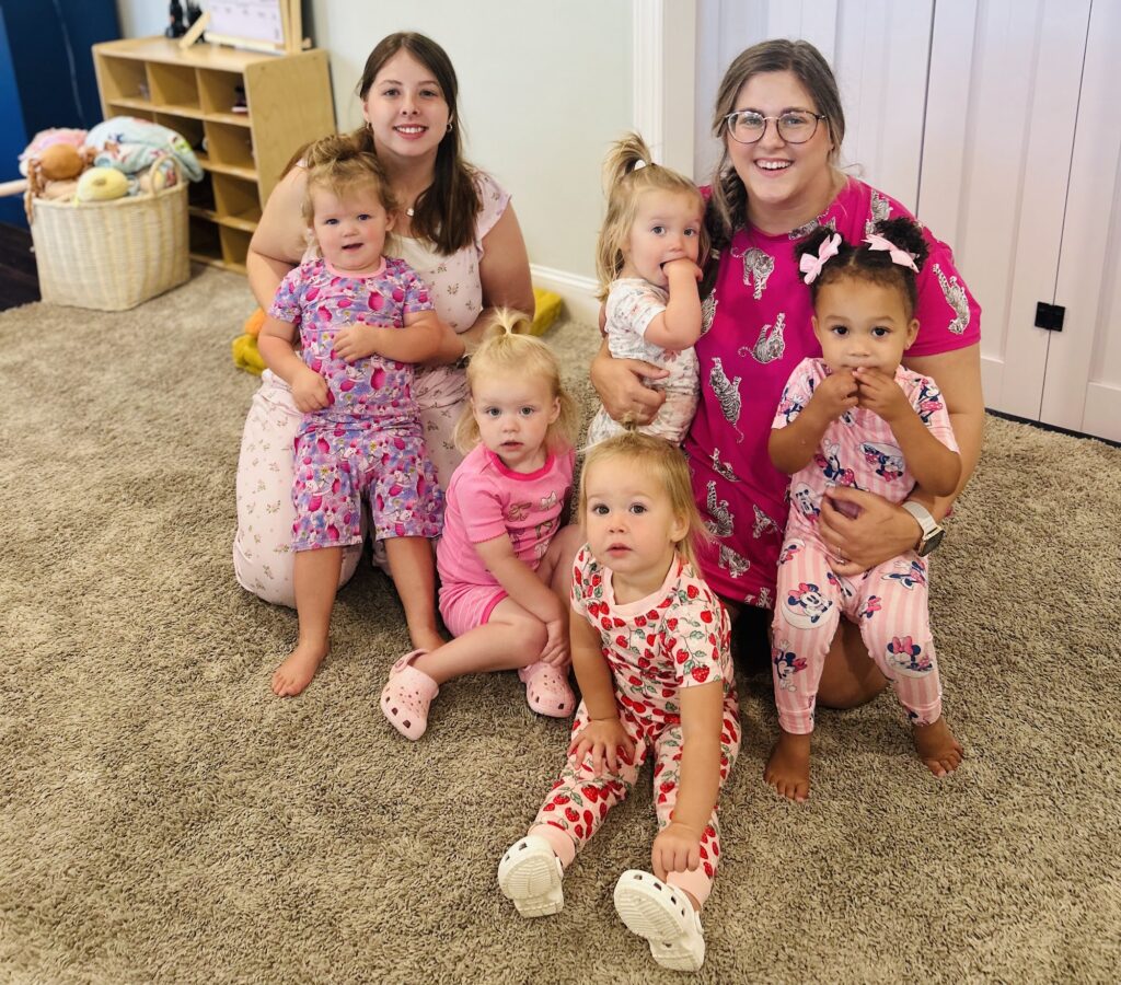 Two Corky teachers sitting on the classroom carpet with a group of smiling toddlers